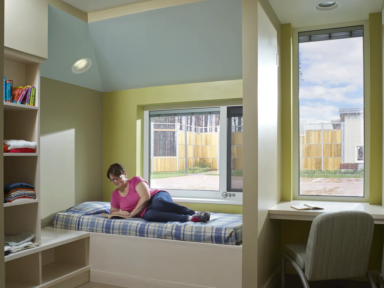 Patient bedroom with a built-in window seat, open shelving and a person resting on the bed