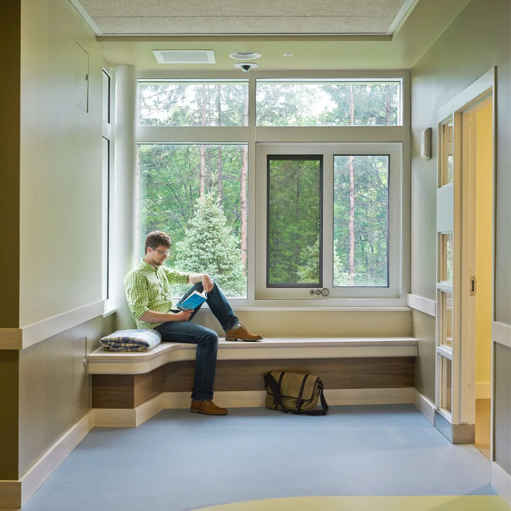 A man reading on a deep timber window seat looking out to conifers